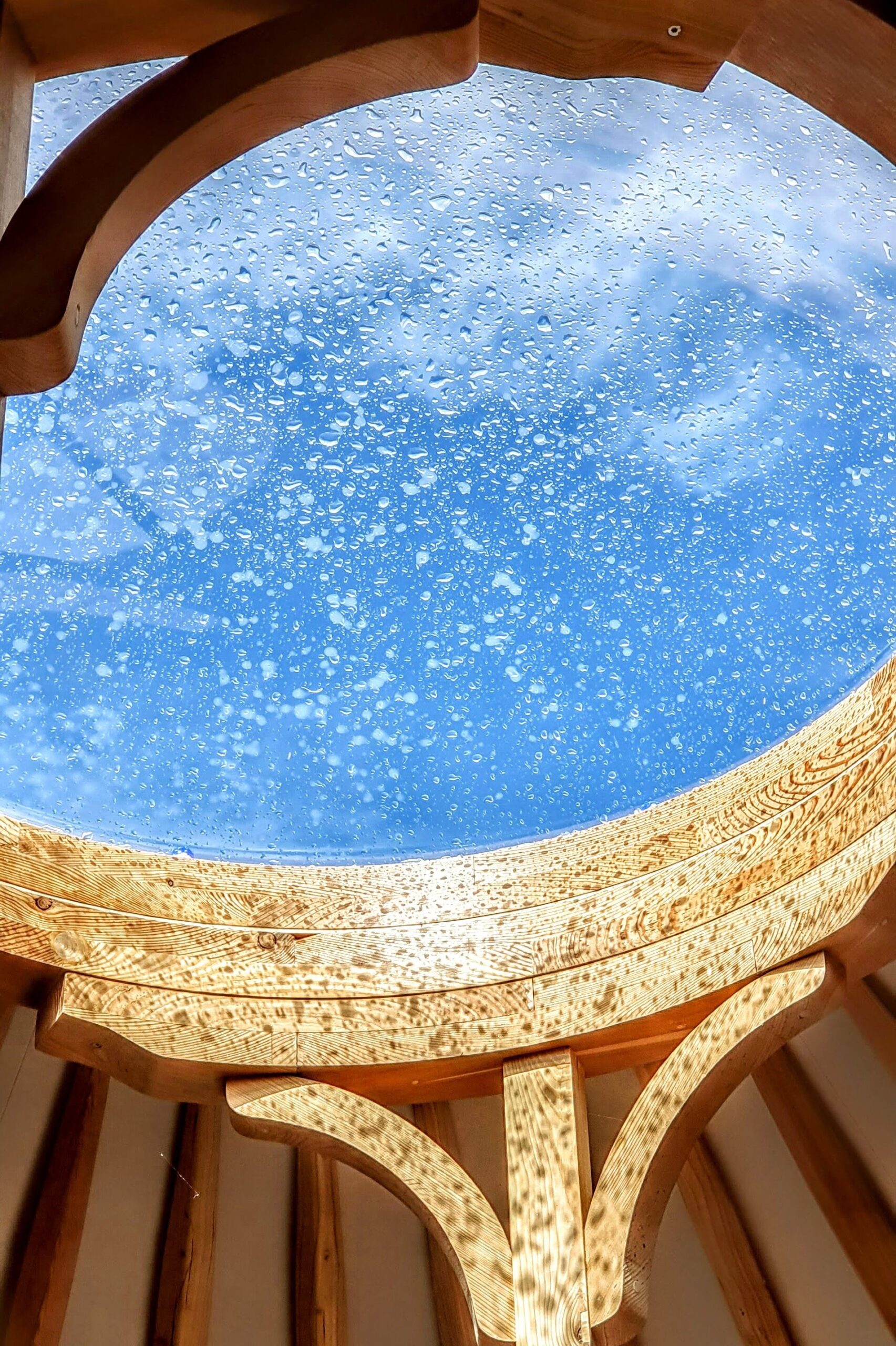 En skylight i en jurt som er dækket af regndråber mens solen skinner ned i jurten. Solskin efter regnen.